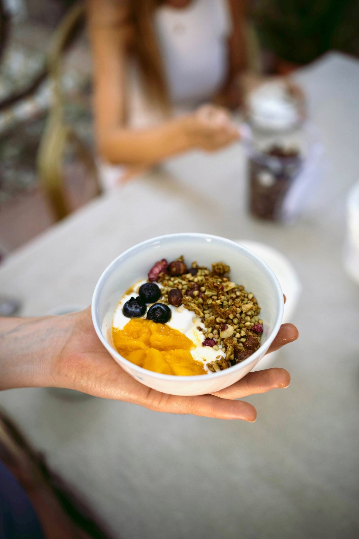 Bol de coco fermentado con mango, arándanos y granola sostenido en la mano
