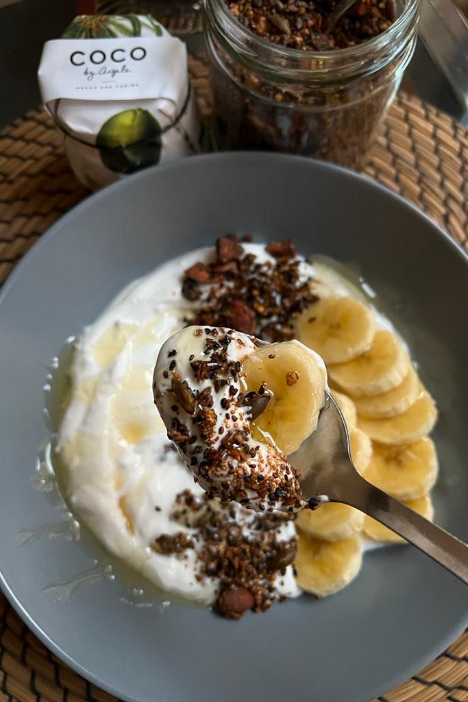 Bol de coco fermentado COCO by Angela con plátano, granola casera de trigo sarraceno y un tarro de granola al fondo
