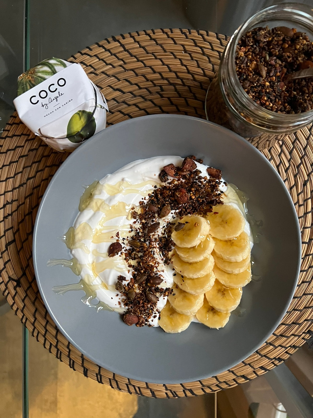 Bol de coco fermentado COCO by Angela con plátano en rodajas, granola de cacao y un hilo de agave