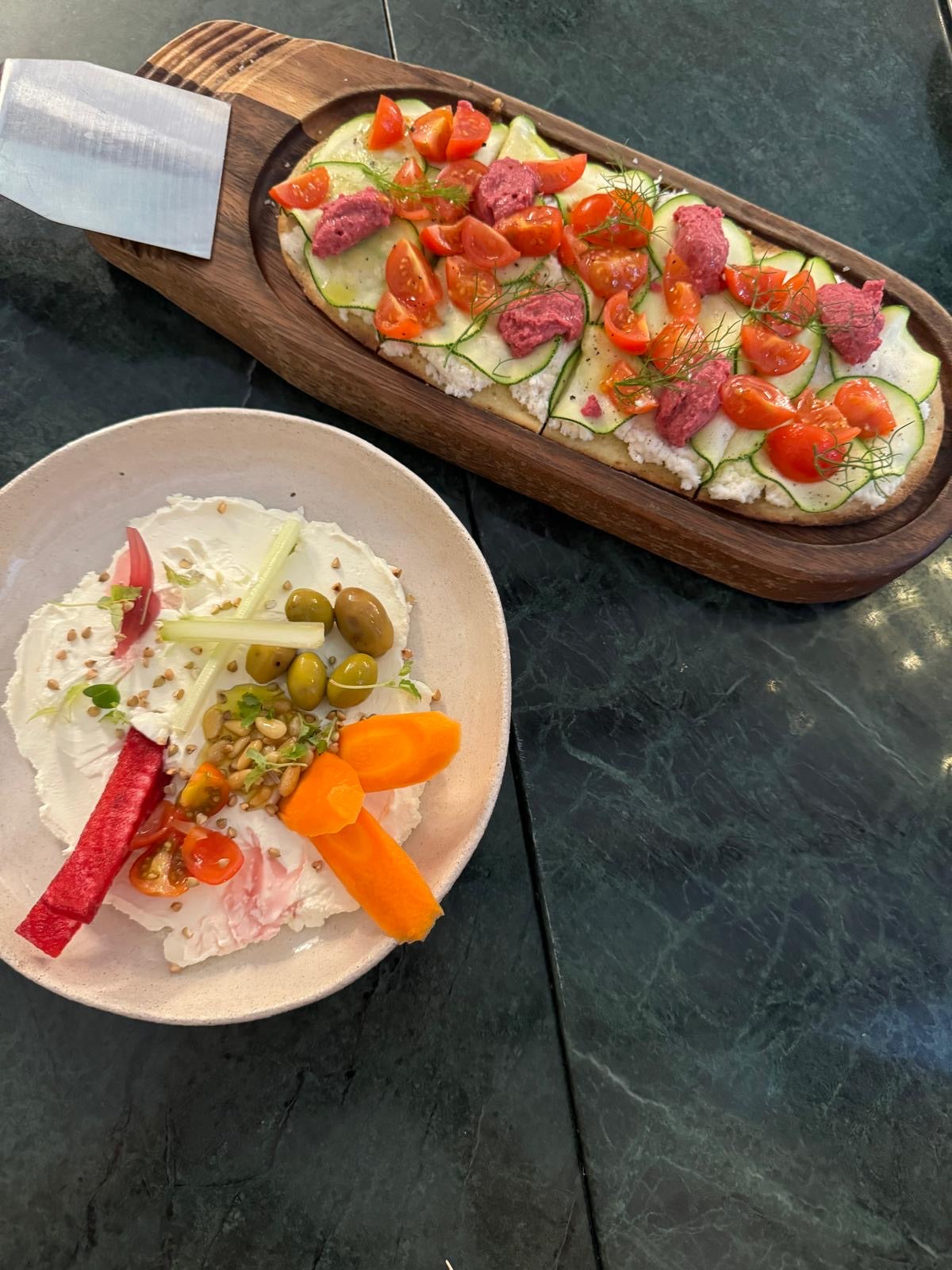 Pan plano con coco fermentado COCO by Angela, calabacín y tomate, junto a un plato de crudités con aceitunas y zanahoria