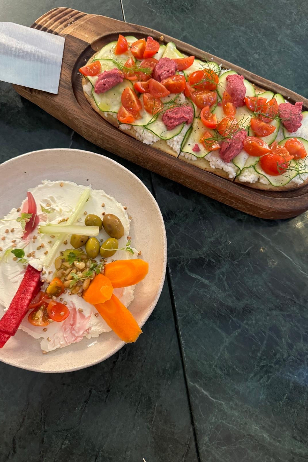 Pan plano con coco fermentado COCO by Angela, calabacín y tomate, junto a un plato de crudités con aceitunas y zanahoria