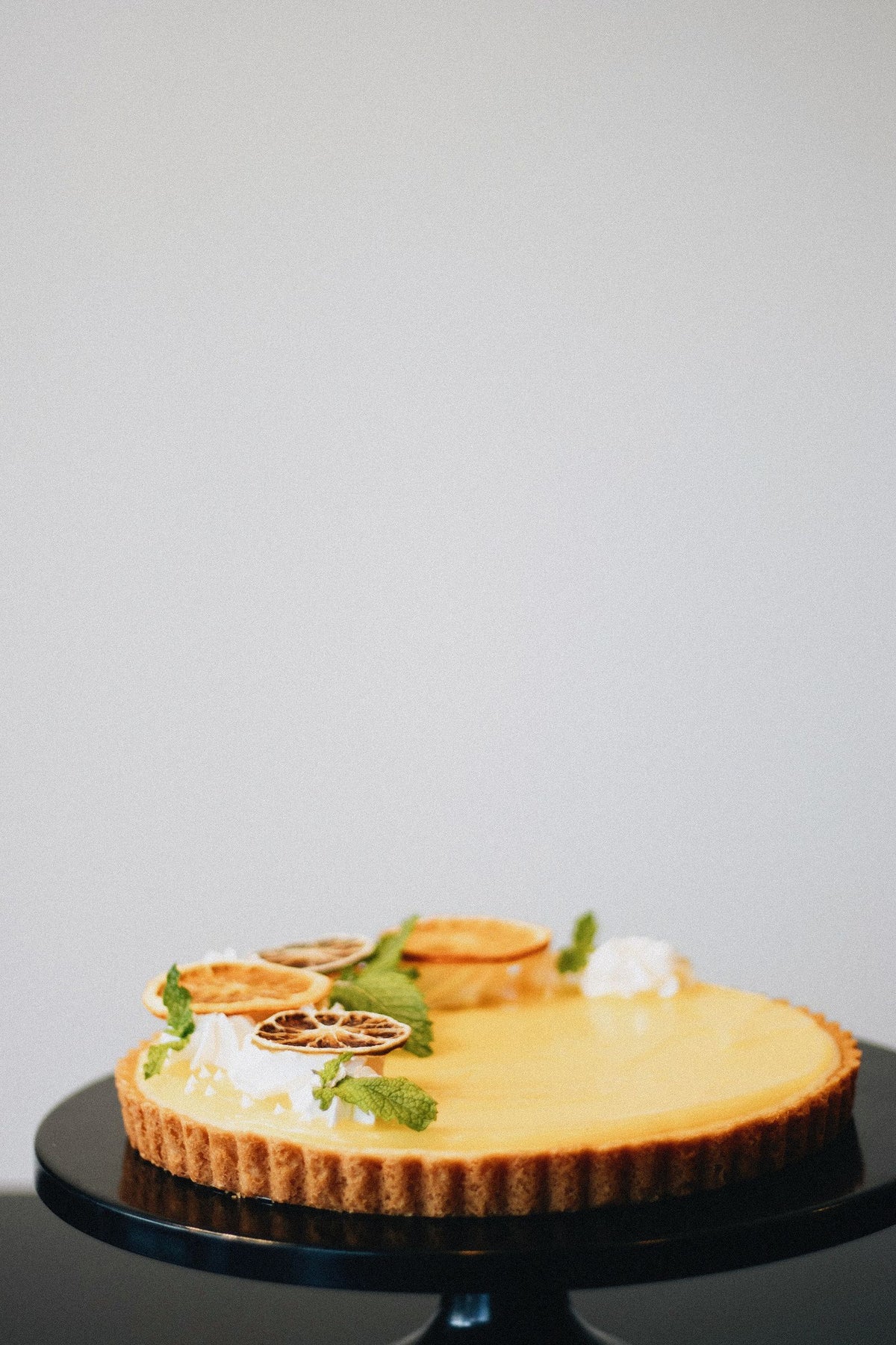 Tarta fría de limón decorada con menta y rodajas de cítricos, sobre un soporte para tartas