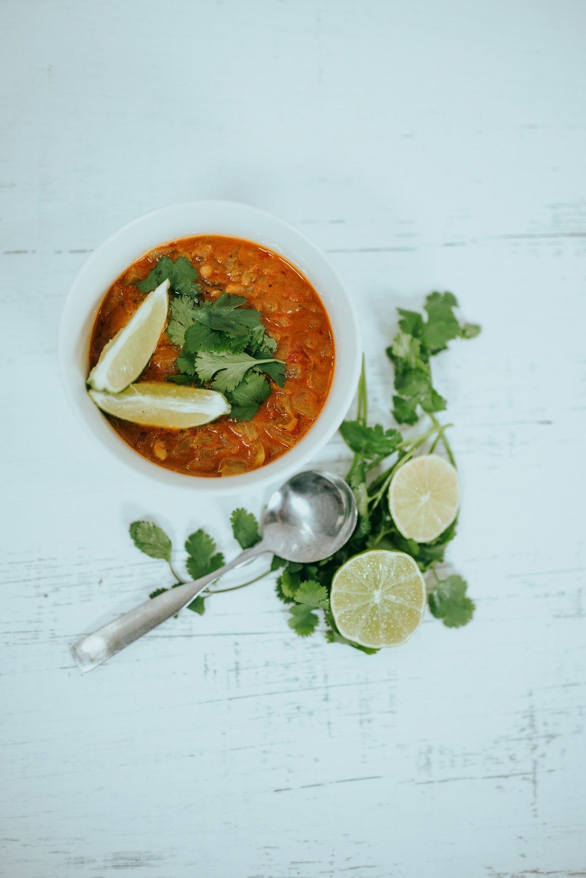 Curry de lentejas rojas en un cuenco blanco con cilantro y gajos de lima